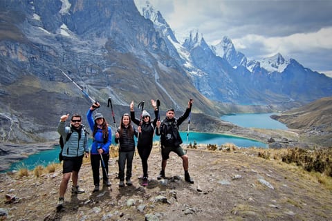 Five trekkers with raised poles at the Three Lakes viewpoint on the Cordillera Huayhuash Mini Trek, three turquoise lakes and the snow walls of the range below them